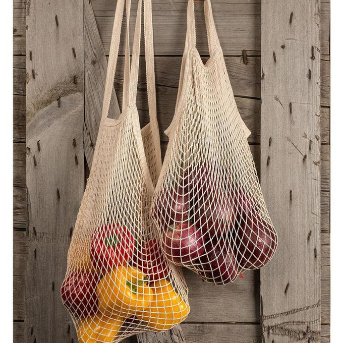 Two natural cotton mesh bags with shoulder handles hanging against rustic wood, filled with fresh red and yellow bell peppers, ideal for Kitchen & Food, Storage and Serving, Best Sellers, and Promo Eligible collections.