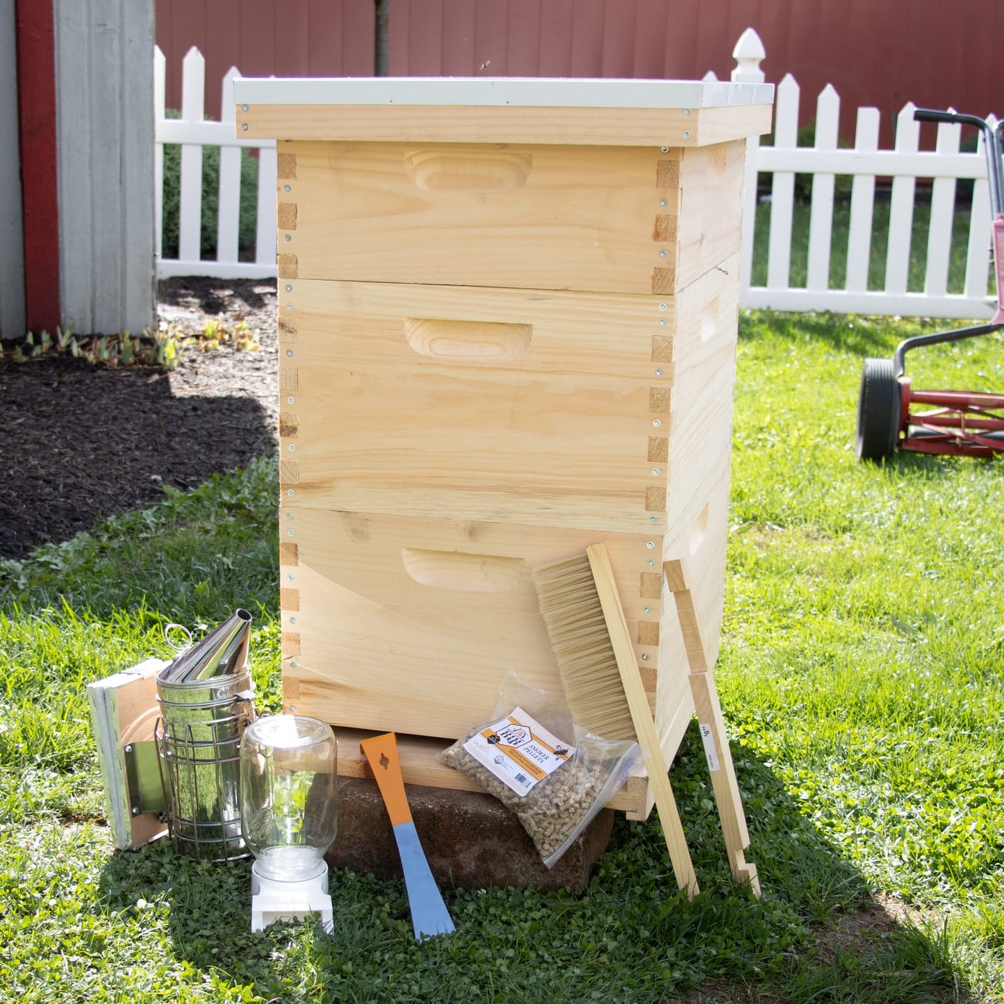 Amish-crafted natural wood 10-frame beehive with essential beekeeping tools including smoker, brush, frame grip, hive tool, and bee feeder, set outdoors on green grass, ideal for Farm, Garden & Tool, 10-Frame Hives and Components, Beekeeping Supplies, Best Sellers, and Promo Eligible collections.