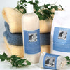 Bottle of handcrafted fabric softener with lavender essential oil placed alongside matching laundry soap and sachets, surrounded by folded towels and green foliage, suitable for Home & Decor, Laundry Supplies, and USA Made collections.