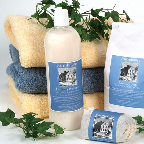 Bottle of handcrafted fabric softener with lavender essential oil placed alongside matching laundry soap and sachets, surrounded by folded towels and green foliage, suitable for Home & Decor, Laundry Supplies, and USA Made collections.