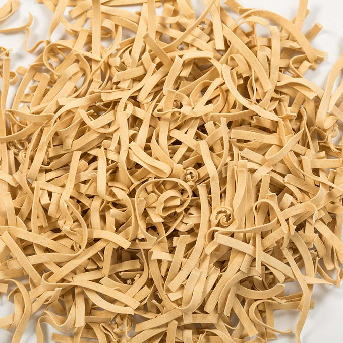 Close-up of uncooked gluten-free homestyle noodles in a loose pile, showcasing their natural beige color and traditional egg noodle texture, part of Kitchen & Food, Pantry, and USA Made collections.