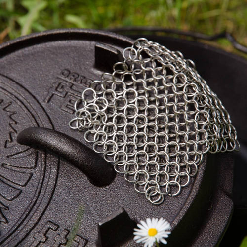 Sturdy stainless steel chainmail scrubber resting on a cast iron pan lid, handcrafted for effective cleaning, featured in Home & Decor, Household Cleaning, and Cleaning Utensils collections.