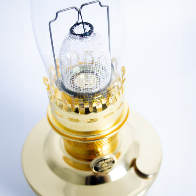 Close-up of a handcrafted brass oil lamp burner with protective mantle in a clear glass chimney, designed for bright, reliable light in farm, garden, and emergency supplies collections.