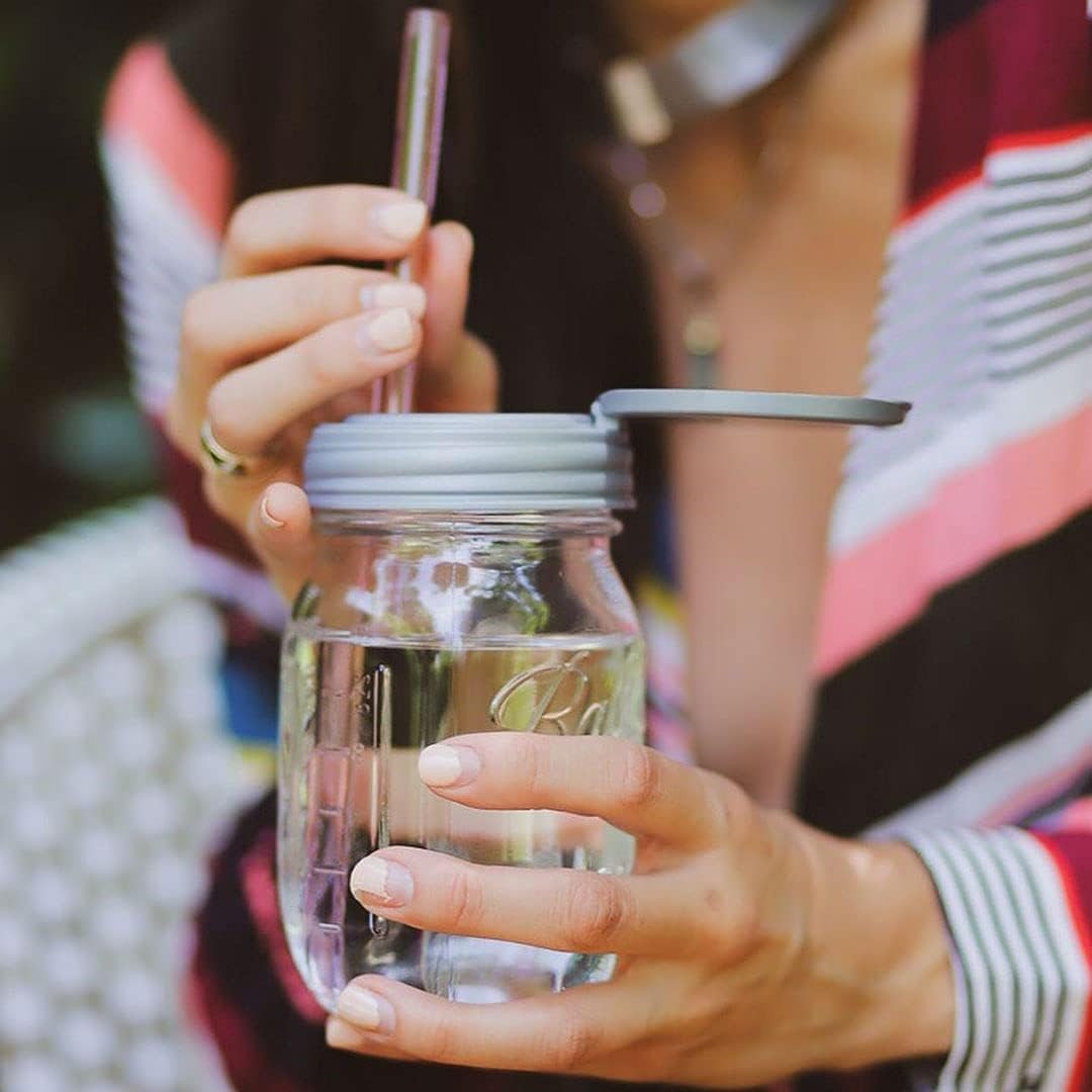 Woman holding a clear glass jar with a gray flip top lid open and a straw inserted, showcasing a handcrafted, reusable lid made in USA for Home & Decor, Kitchen Gadgets, and Storage and Serving collections.