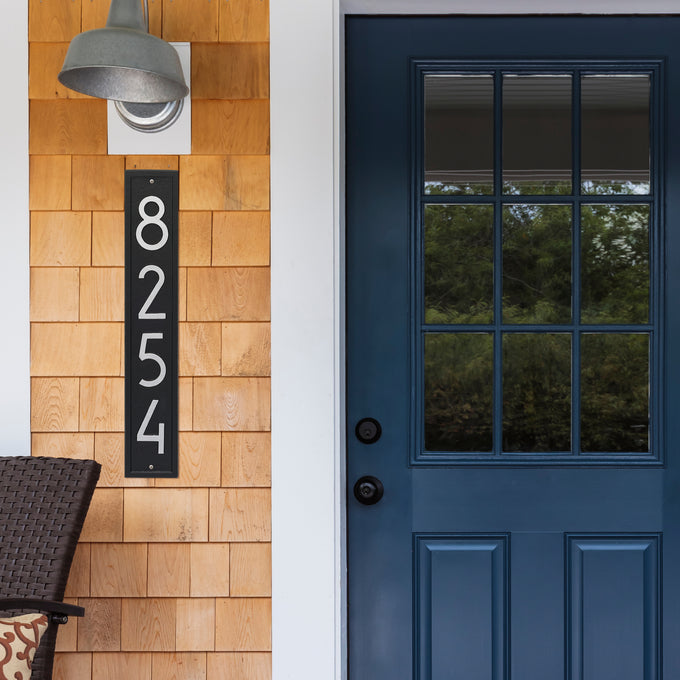 Slim vertical black and silver custom address plaque with modern white numbers mounted on wooden siding beside a blue door, handcrafted in USA, featured in Home & Decor and Mailboxes and Address Signs collections.