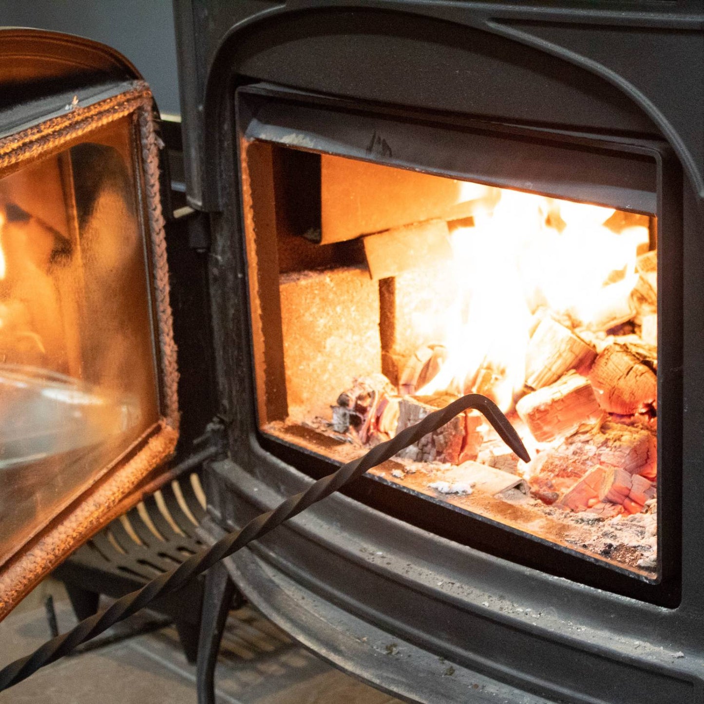 Handcrafted steel fire poker with a loop handle, Amish made in the USA, shown positioned in a burning wood stove, part of Stoves, Hearth Accessories, and Best Sellers collections.