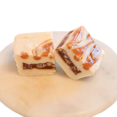 Two handcrafted creamy white and caramel swirl fudge pieces with walnut layers on a smooth white marble plate, featured in Kitchen & Food, Snacks and Sweets, USA Made, Best Sellers, and Promo Eligible collections.