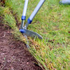 Close-up of garden edging shears with sharp steel blades and tubular handles trimming a clean edge between soil and grass in a lawncare setting, ideal for farm and garden use.