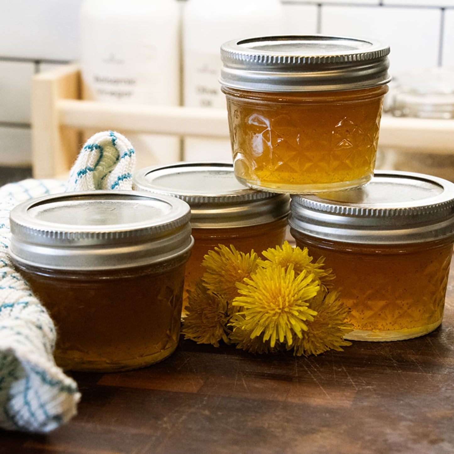Set of clear quilted glass jelly jars with silver metal lids filled with amber preserves, displayed with yellow flowers and a kitchen towel, crafted for food preservation and canning, part of USA Made and Kitchen & Food collections.