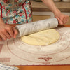 Hands using a smooth marble rolling pin to roll out dough on a floured pastry mat in a warm kitchen environment, part of Kitchen & Food, Cookware, and Baking Supplies collections.