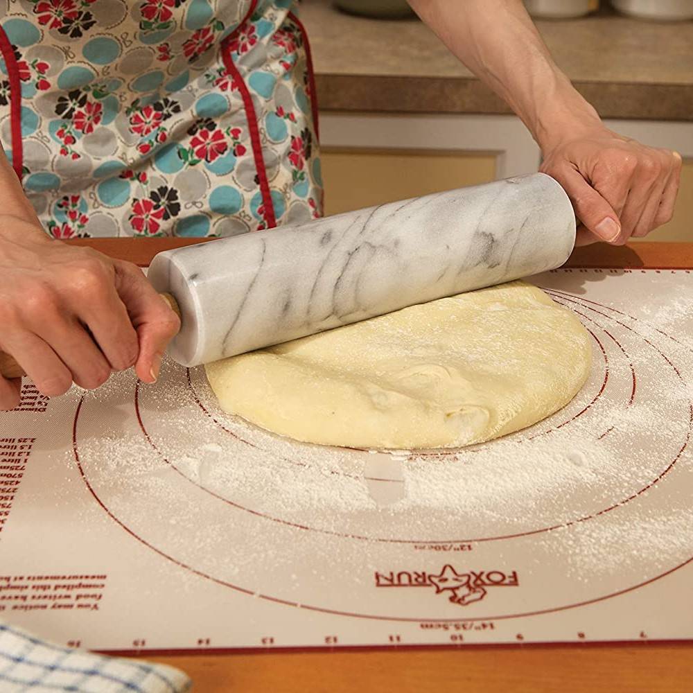 Hands using a smooth marble rolling pin to roll out dough on a floured pastry mat in a warm kitchen environment, part of Kitchen & Food, Cookware, and Baking Supplies collections.