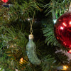 Green pickle-shaped ornament hanging from a gold string on a Christmas tree, part of a handcrafted holiday decor collection featured in Home & Decor and Best Sellers.