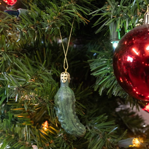 Green pickle-shaped ornament hanging from a gold string on a Christmas tree, part of a handcrafted holiday decor collection featured in Home & Decor and Best Sellers.