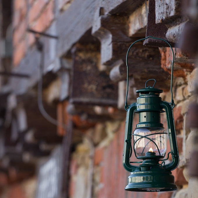 Handcrafted green galvanized oil lantern with thermal heat-resistant SUPRAX globe, glowing softly while hanging from a rustic wooden beam, ideal for Camping, Lamps & Lighting, and Emergency Supplies collections.