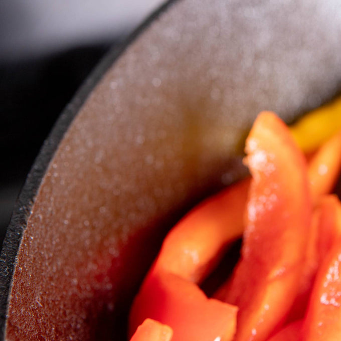 Close-up of handcrafted cast iron skillet cooking vibrant red and yellow bell pepper slices, highlighting seasoned surface and durable USA-made craftsmanship in Kitchen & Food collections.