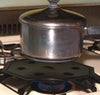 Steel heat diffuser with multiple vent holes placed on a gas stove burner under a covered saucepan, designed for consistent low-heat simmering in Kitchen & Food and Cooking and Baking Helpers collections.