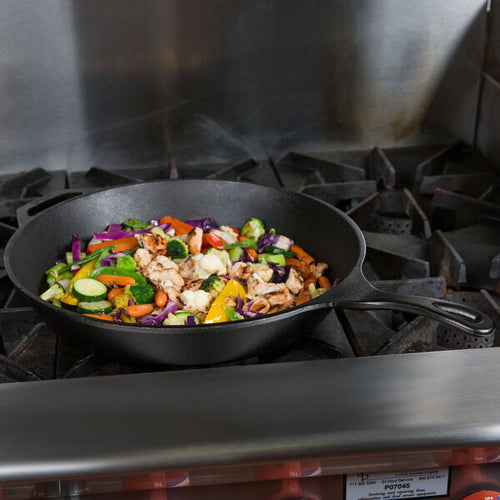 Handcrafted Lodge Classic Cast Iron Skillet cooking a colorful mix of fresh vegetables and chicken on a commercial stove, showcasing unparalleled heat retention for Kitchen & Food, Cookware, Cast Iron, Best Sellers, Promo Eligible collections.
