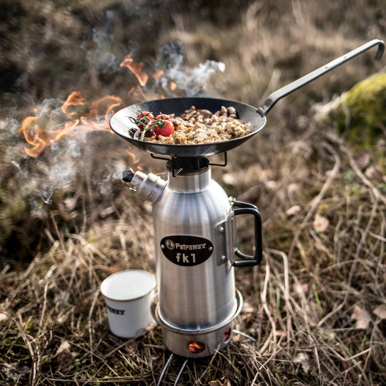 Outdoor stainless steel fire kettle with a black cast iron frying pan on top, cooking food over open flames in natural setting, featured in Kitchen & Food, Cookware, Cast Iron, and Best Sellers collections.