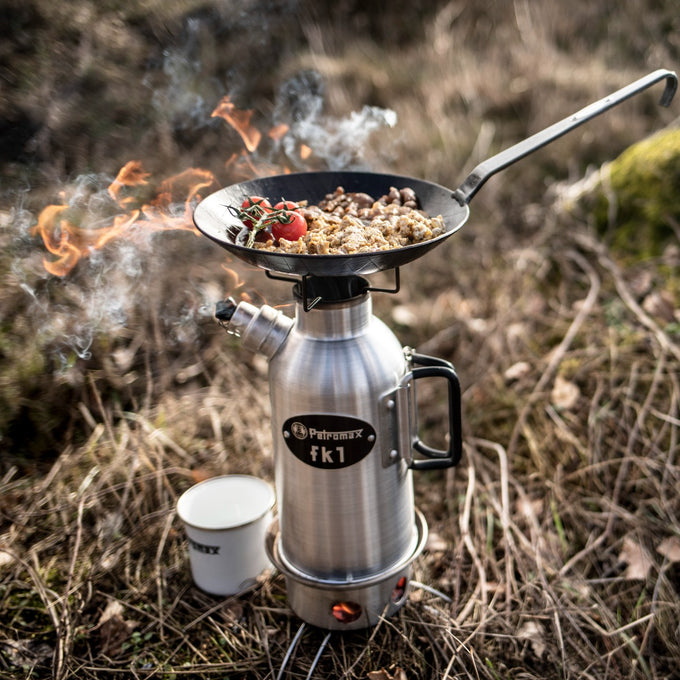 Outdoor stainless steel fire kettle with a black cast iron frying pan on top, cooking food over open flames in natural setting, featured in Kitchen & Food, Cookware, Cast Iron, and Best Sellers collections.