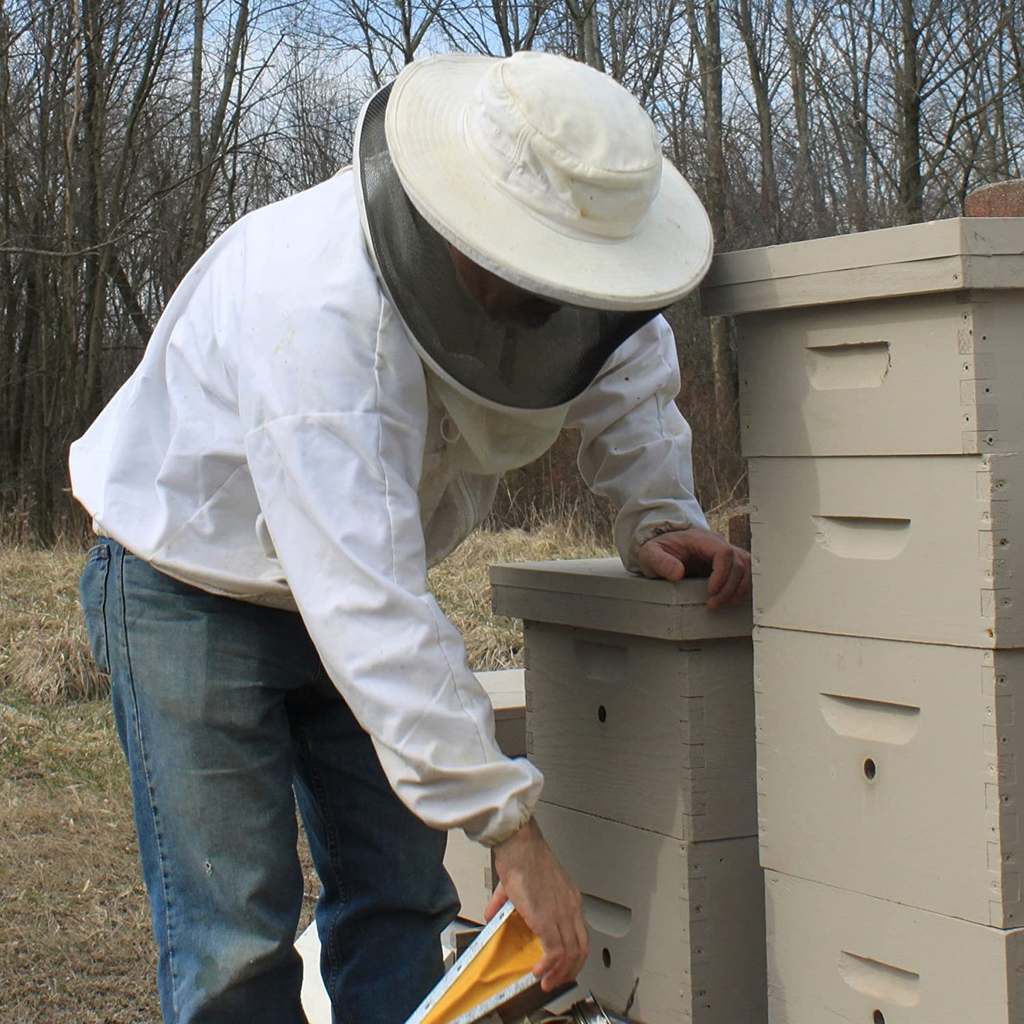 Beekeeper in protective clothing inspecting wooden beehives outdoors, illustrating natural honey sourcing and handcrafted, USA made products in Health & Wellness and Soaps collections.