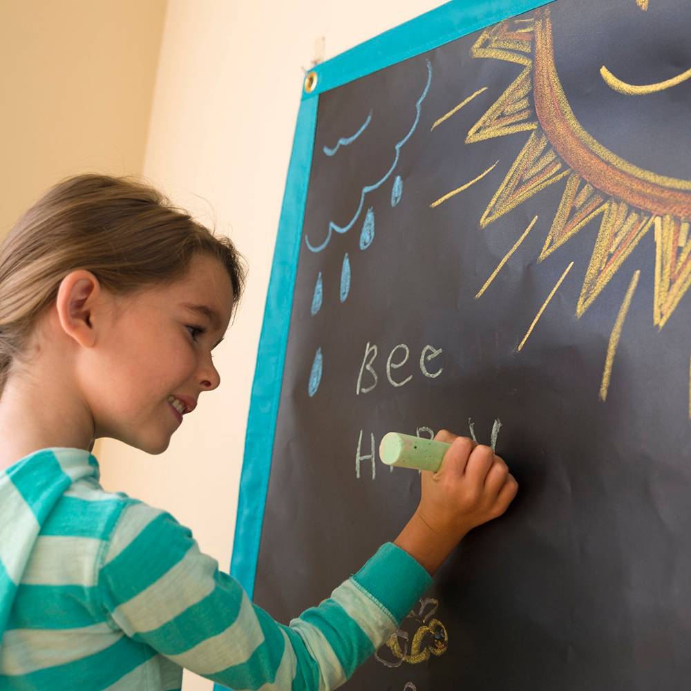 Young girl drawing with chalk on a handcrafted roll-up chalk mat hung on a wall, featured in Children's Toys, Indoor Play, and Best Sellers collections.