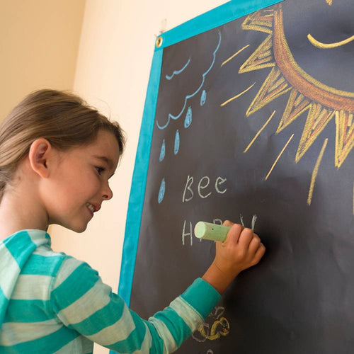 Young girl drawing with chalk on a handcrafted roll-up chalk mat hung on a wall, featured in Children's Toys, Indoor Play, and Best Sellers collections.