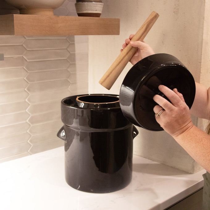 Handcrafted black fermenting crock with matching lid and wooden stomper being used on a kitchen counter, ideal for Kitchen & Food, Food Preservation, and Fermenting and Pickling collections.