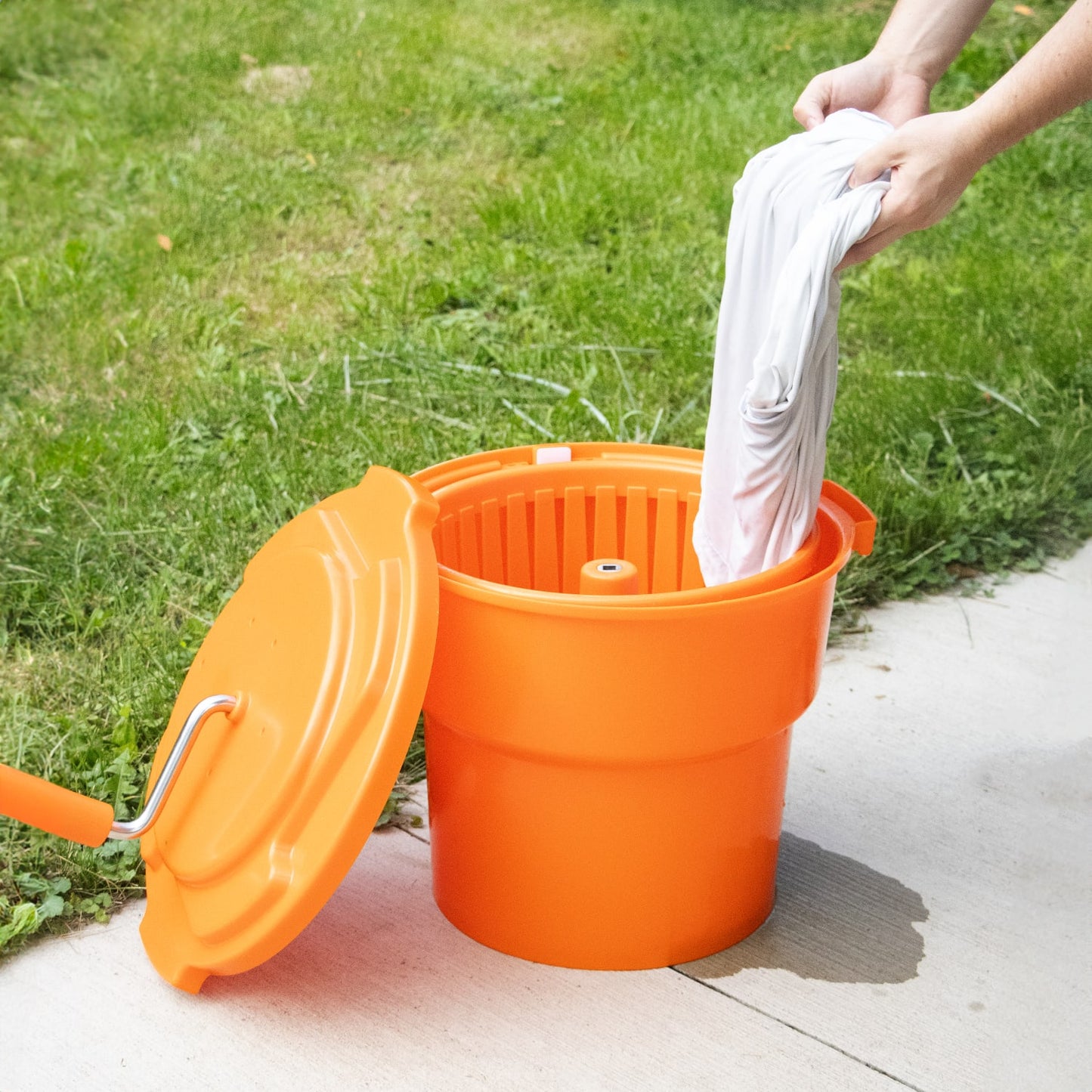 Handcrafted bright orange hand-powered laundry spinner with crank handle and removable lid, used outdoors to quickly remove water from clothing, featured in Laundry Supplies and Home & Decor collections.