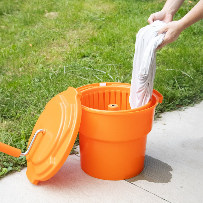 Handcrafted bright orange hand-powered laundry spinner with crank handle and removable lid, used outdoors to quickly remove water from clothing, featured in Laundry Supplies and Home & Decor collections.