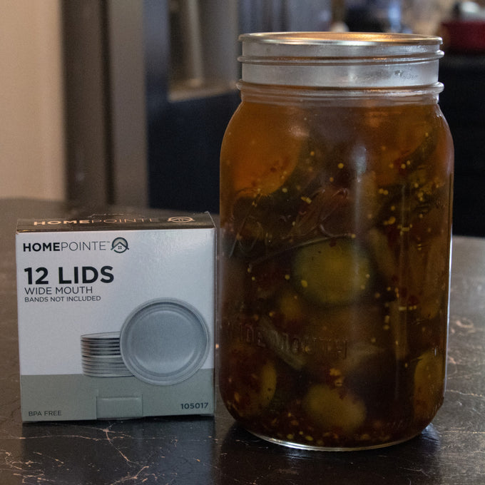 Glass jar filled with homemade pickles sealed with a wide-mouth metal canning lid, next to a box of 12 BPA-free sealing lids, ideal for Kitchen & Food, Food Preservation, and Canning collections.