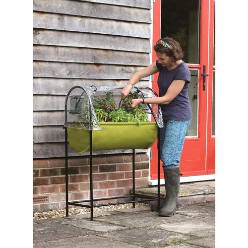 Woman tending to plants in a green fabric raised garden bed with a clear polyethylene greenhouse cover and black metal frame, suitable for patios and small outdoor spaces in Farm, Garden & Tool and Garden Accessories collections.