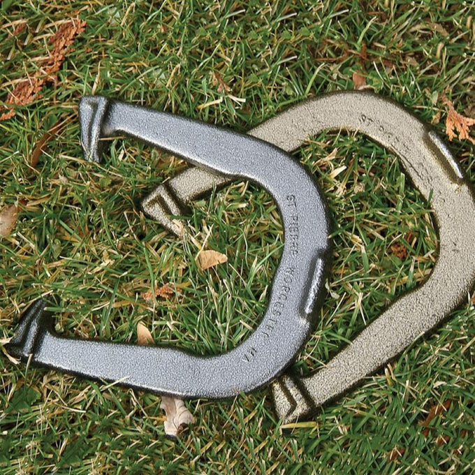 Two solid steel horseshoes, one silver and one gold-toned, laid on grass representing a premium, durable set made in USA, featured in lawn games and best sellers collections.