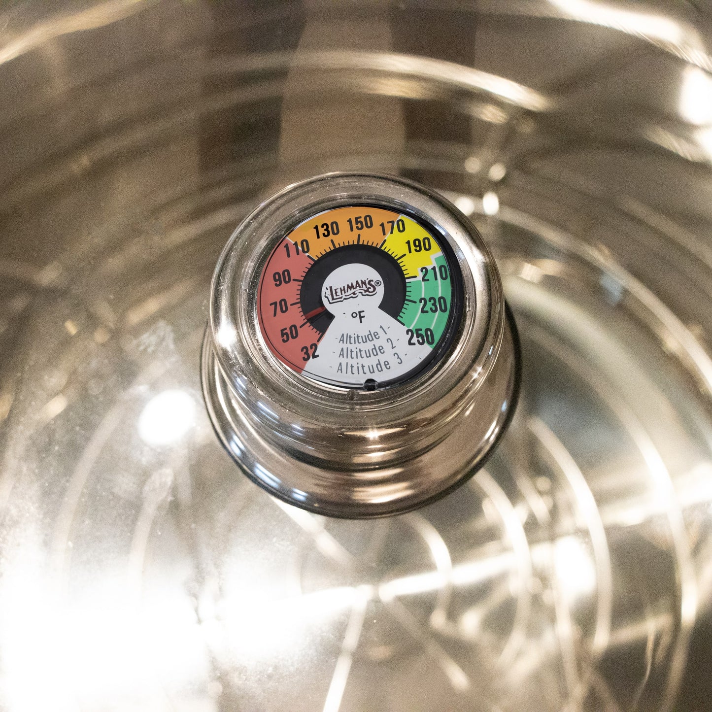 Close-up of Lehman's built-in temperature gauge on a stainless steel canner lid, showing a colorful dial for precise heat monitoring, featured in Kitchen & Food and Food Preservation collections.