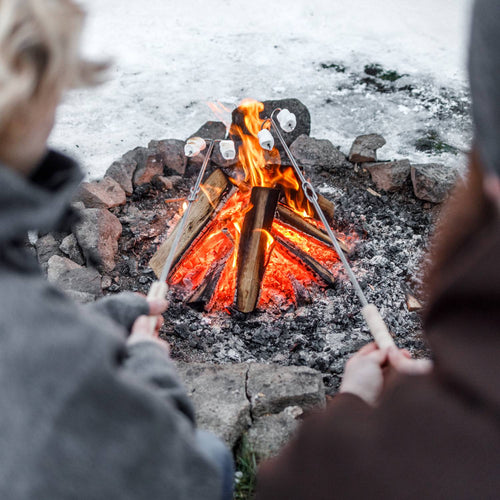 Handcrafted campfire skewer with adjustable handle roasting marshmallows over a stone fire pit in a snowy outdoor setting, ideal for Farm, Garden & Tool, Camping, Best Sellers, and Promo Eligible collections.