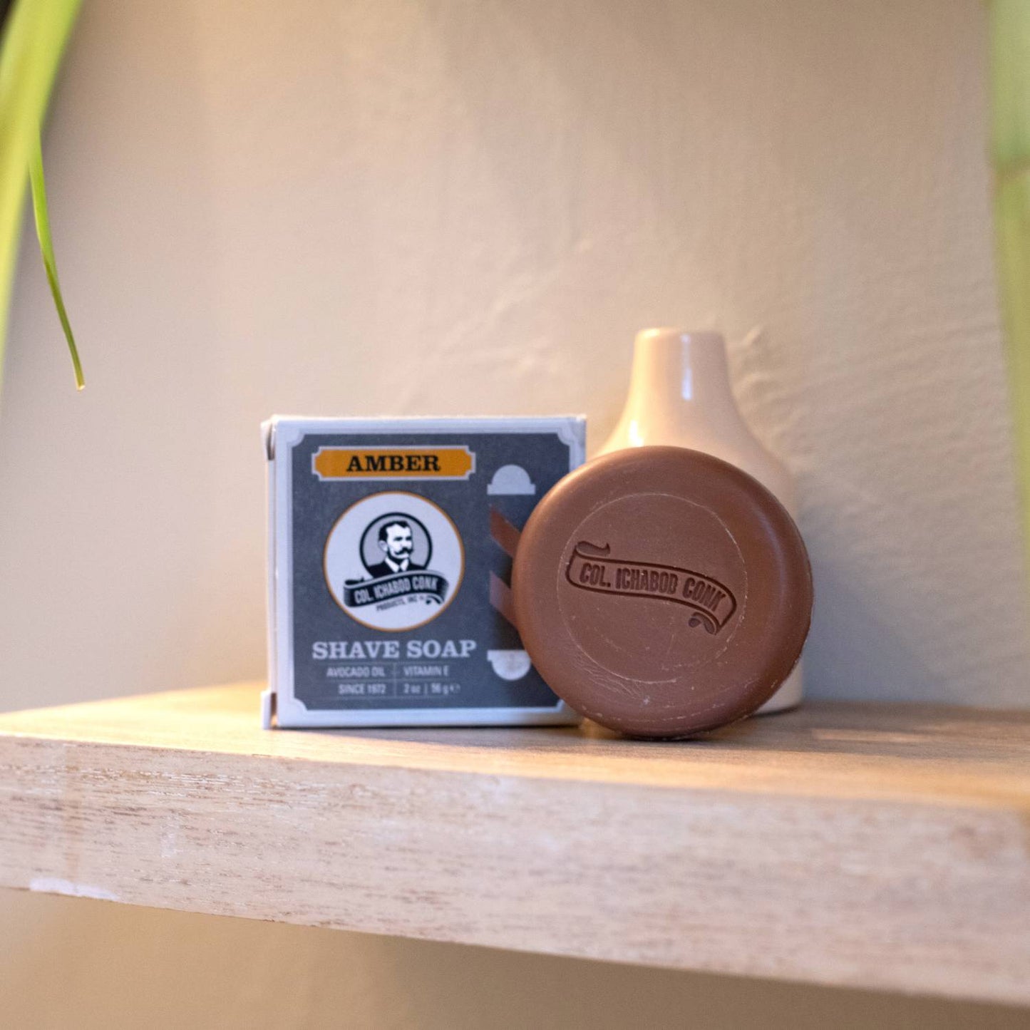 Amber-colored moist shaving soap bar embossed with brand name beside its original box packaging, styled simply on a wooden shelf, featured in Health & Wellness, Grooming and Personal Hygiene, Soaps and Soapmaking, USA Made, Best Sellers, and Promo Eligible collections.