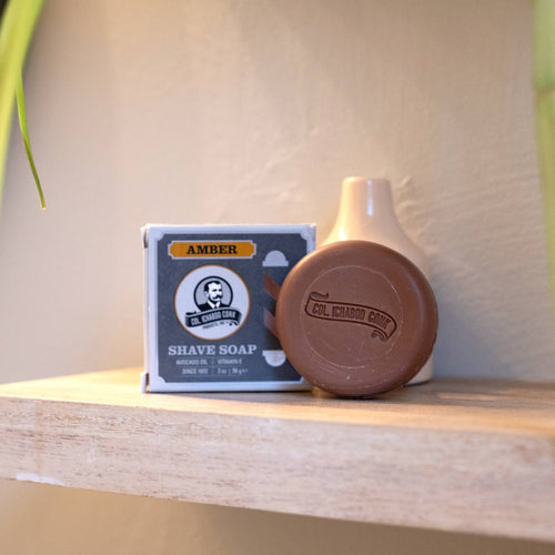 Amber-colored moist shaving soap bar embossed with brand name beside its original box packaging, styled simply on a wooden shelf, featured in Health & Wellness, Grooming and Personal Hygiene, Soaps and Soapmaking, USA Made, Best Sellers, and Promo Eligible collections.