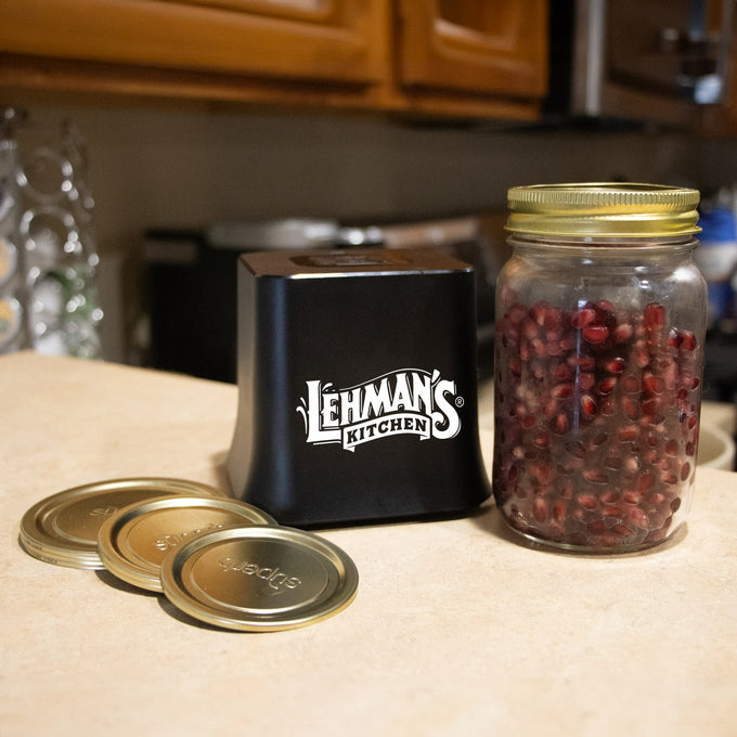 Black cordless vacuum sealer unit with digital display beside a mason jar filled with pomegranate seeds and extra gold-toned lids on a kitchen counter, featured in Kitchen & Food and Best Sellers collections