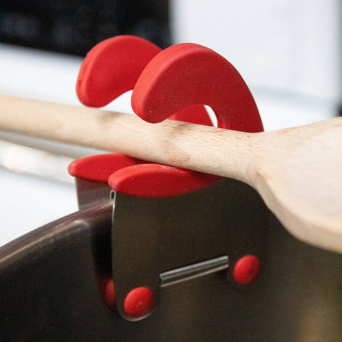 Sturdy pot clip with red silicone grips holding a wooden spoon securely on the side of a pot, designed to keep utensils accessible and off kitchen surfaces in Kitchen Gadgets and Cooking Helpers.