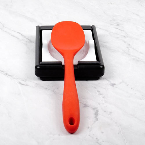 Plastic frame with white porcelain rest holding a bright orange cooking spoon, designed as a compact two-in-one kitchen gadget for spoon and lid support in Kitchen & Food collections.