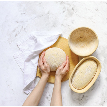 Hands holding a round sourdough dough ball next to handcrafted oval and round proofing baskets with removable liners on a floured surface, ideal for Kitchen & Food and Baking Supplies.