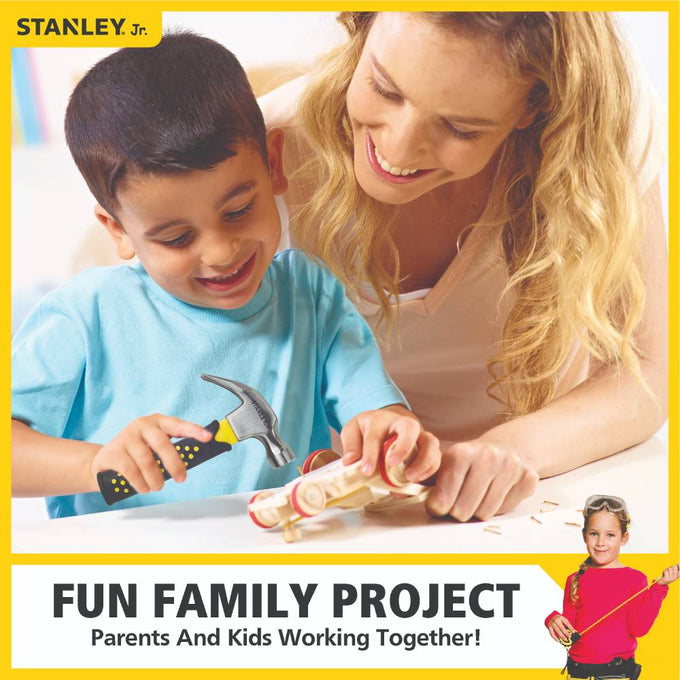 Smiling young boy using a child-sized hammer to work on a wooden project with his mother, promoting family bonding and indoor play with real hand tools.