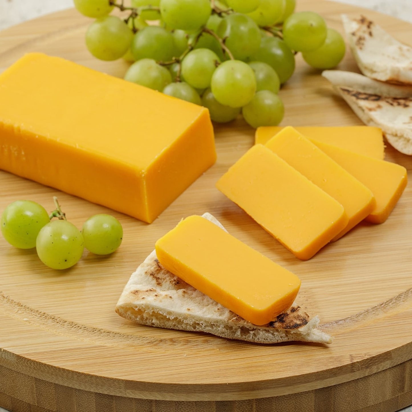 Two 8-ounce handcrafted shelf-stable cheese food blocks, sliced and served on flatbread with green grapes on a round board, ideal for Kitchen & Food, Pantry, Snacks and Sweets, USA Made, and Best Sellers collections.