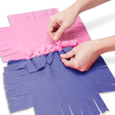 Hands tying fringed pink and purple super-soft fleece pieces together to create a colorful, oversized flower quilt, part of children's arts and crafts and best sellers collections.