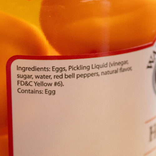 Close-up of a product label detailing ingredients of hot pickled eggs in a glass jar, featuring eggs, pickling liquid with vinegar and red bell peppers, from USA Made Kitchen & Food collections.
