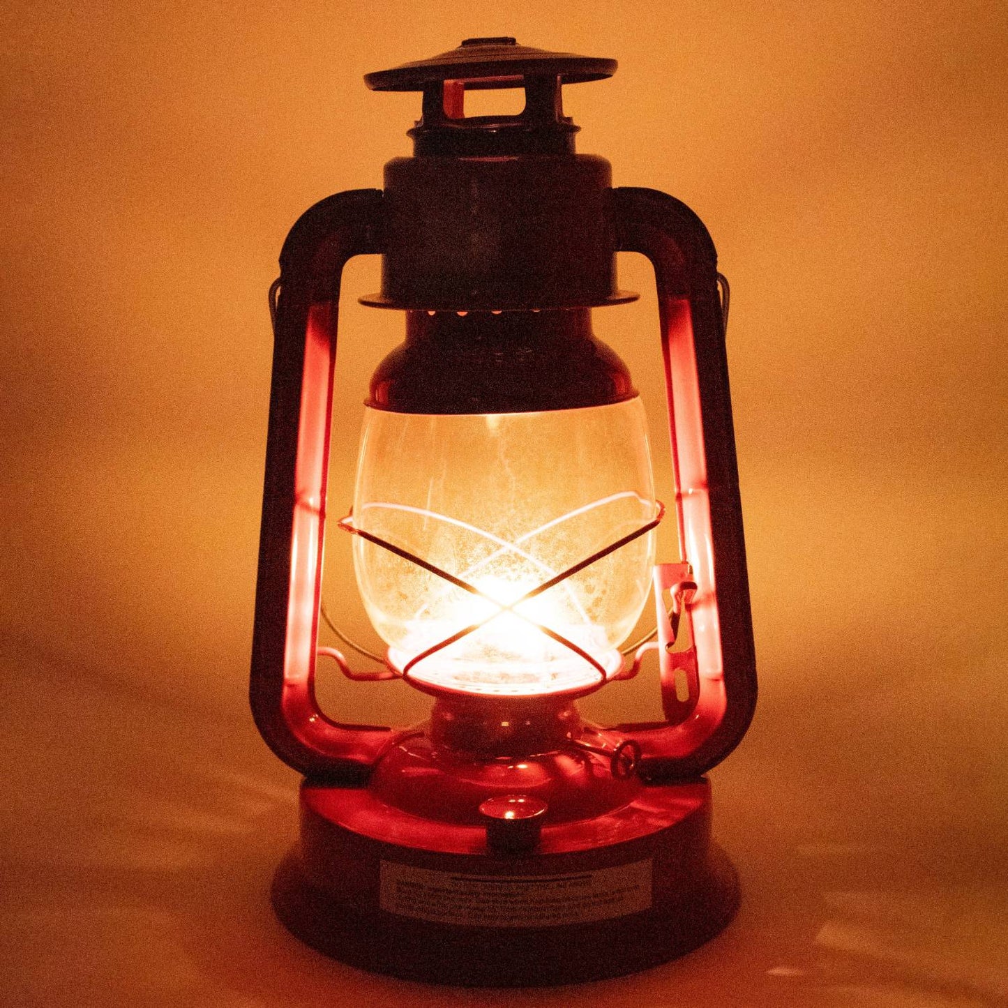 Handcrafted red metal lantern with glowing flame inside frosted glass globe, designed for outdoor use in camping, pest control, farm, garden, and emergency lighting collections.