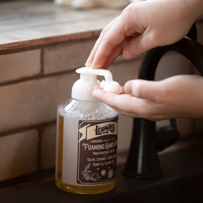 Hand dispensing natural foaming hand soap from clear bottle with pump top, featuring moisturizing formula with olive, coconut, honey, and jojoba oils in a Health & Wellness and Grooming collection.