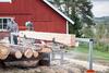 Portable chainsaw mill in use cutting large logs into lumber outdoors near a red barn, ideal for Farm, Garden & Tool, Wood Cutting and Hauling, and Best Sellers collections.