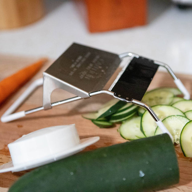 Handcrafted vegetable slicer with stainless steel blade slicing thin cucumber rounds on a wooden cutting board, ideal for Kitchen & Food, Food Prep, Choppers and Cutters, Best Sellers, and Promo Eligible collections.