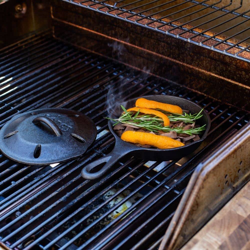 Small seasoned cast iron skillet on gas grill with fresh rosemary and orange peel, steaming under a vented lid, featured in Kitchen & Food, Cookware, Cast Iron, USA Made, and Best Sellers collections.
