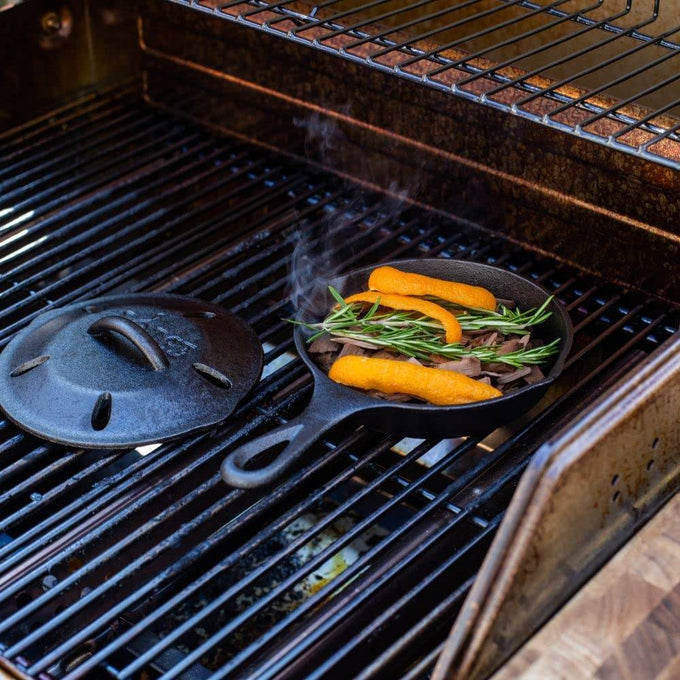 Small seasoned cast iron skillet on gas grill with fresh rosemary and orange peel, steaming under a vented lid, featured in Kitchen & Food, Cookware, Cast Iron, USA Made, and Best Sellers collections.